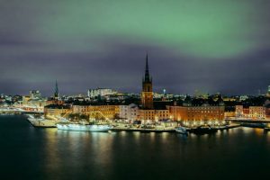 Stockholms stadssiluett på kvällen med grönt norrsken över Gamla stan och Riddarholmen.
