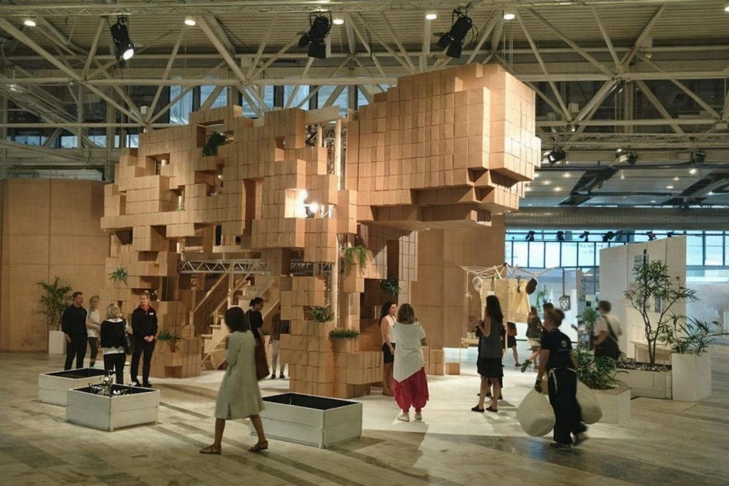Människor i en stor hall med en installation av träblock som påminner om ett konferensrum