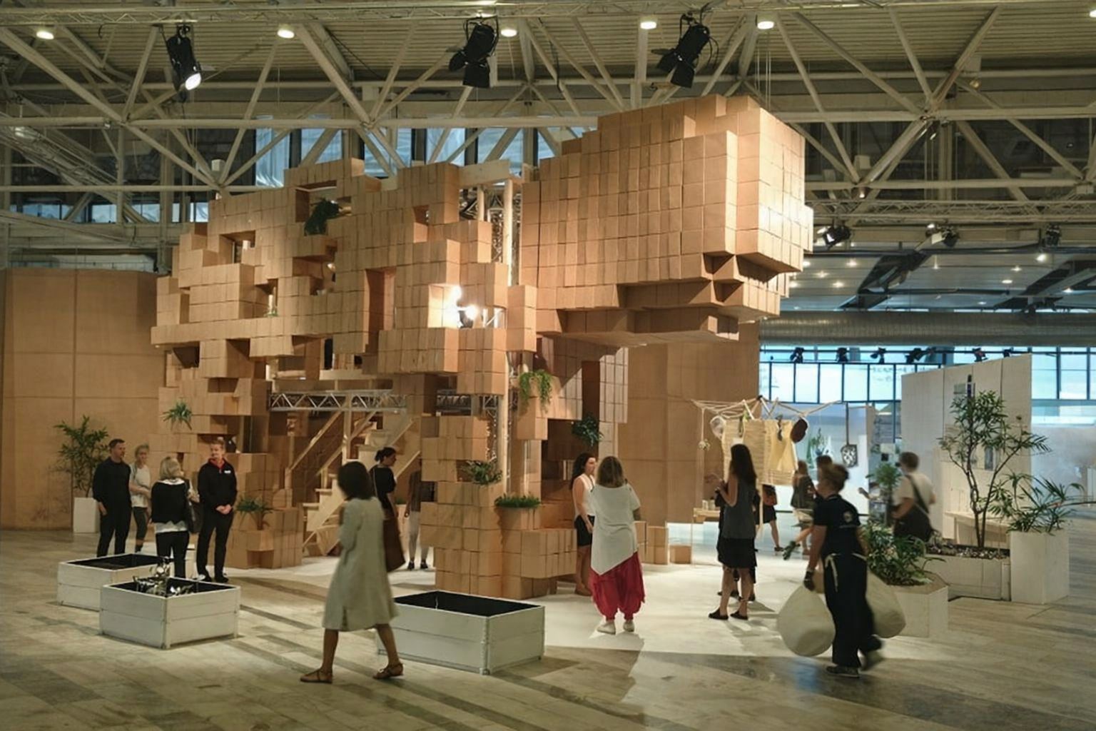 Människor i en stor hall med en installation av träblock som påminner om ett konferensrum