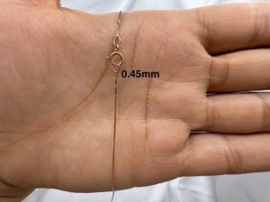 Närbild av ett tunt guldfärgat halsband med fjäderlås mot en handflata.